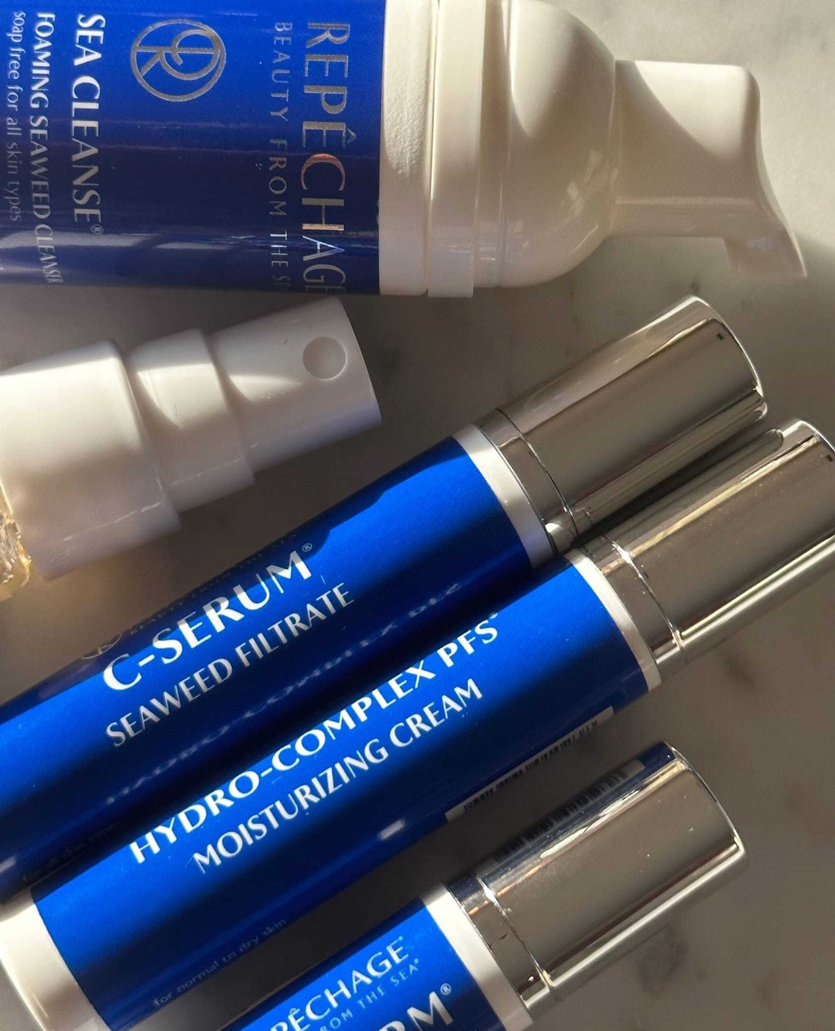 Skincare products with blue labels on a marble surface, including serum and moisturizing cream.
